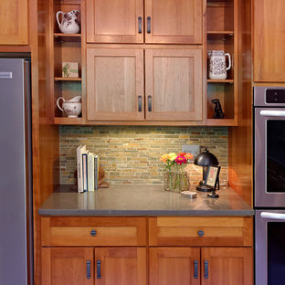 Cette photo montre une très grand cuisine américaine craftsman avec un évier intégré, un placard à porte shaker, des portes de placard en bois brun, un plan de travail en surface solide, une crédence verte, une crédence en carrelage de pierre, un électroménager en acier inoxydable, un sol en carrelage de porcelaine et un îlot central.