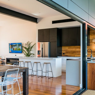 Photo of a mid-sized contemporary l-shaped open plan kitchen in Sydney with quartz benchtops, black appliances, light hardwood floors, with island, white benchtop, flat-panel cabinets, black cabinets, brown splashback, timber splashback and brown floor.