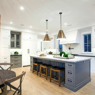 This is an example of an eclectic open plan kitchen in Orange County with grey cabinets, marble benchtops, white splashback, glass tile splashback, stainless steel appliances, light hardwood floors and with island.