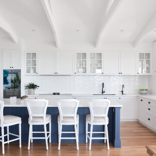 Design ideas for a large beach style l-shaped eat-in kitchen in Brisbane with an undermount sink, shaker cabinets, white cabinets, white splashback, panelled appliances, with island, beige floor and white benchtop.