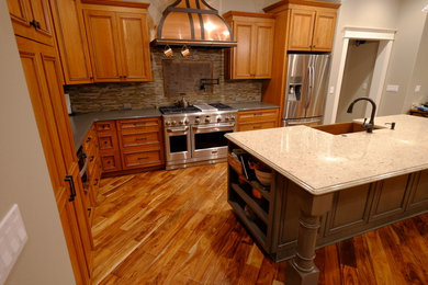 Large arts and crafts l-shaped medium tone wood floor and brown floor eat-in kitchen photo in Sacramento with a farmhouse sink, shaker cabinets, medium tone wood cabinets, solid surface countertops, brown backsplash, stone tile backsplash, stainless steel appliances and an island