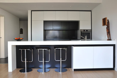 Diseño de cocina comedor minimalista pequeña con fregadero encastrado, puertas de armario blancas, salpicadero negro, suelo de baldosas de porcelana y una isla