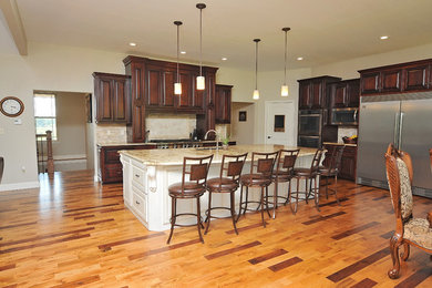 Photo of a contemporary kitchen/diner in Kansas City with recessed-panel cabinets, dark wood cabinets, granite worktops, beige splashback, stone slab splashback, stainless steel appliances, light hardwood flooring and an island.