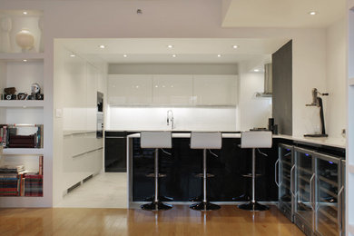 Mid-sized minimalist eat-in kitchen photo in New York with glass-front cabinets, white cabinets, white backsplash, stainless steel appliances, a peninsula, white countertops and glass tile backsplash