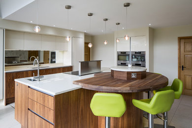 This is an example of a large modern l-shaped open plan kitchen in Hertfordshire with a built-in sink, shaker cabinets, medium wood cabinets, granite worktops, metallic splashback, mirror splashback, stainless steel appliances, ceramic flooring, multiple islands and white floors.