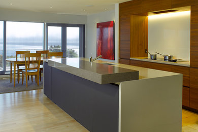 Large contemporary l-shaped open plan kitchen in San Francisco with a submerged sink, flat-panel cabinets, medium wood cabinets, composite countertops, white splashback, glass sheet splashback, integrated appliances, light hardwood flooring, an island and beige floors.
