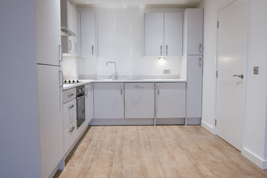 This is an example of a small modern l-shaped enclosed kitchen in London with a double-bowl sink, flat-panel cabinets, white cabinets, laminate countertops, black appliances, no island and white worktops.