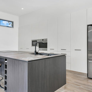 Photo of a contemporary galley kitchen in Cairns with an undermount sink, flat-panel cabinets, white cabinets, stainless steel appliances, light hardwood floors, a peninsula, beige floor and grey benchtop.