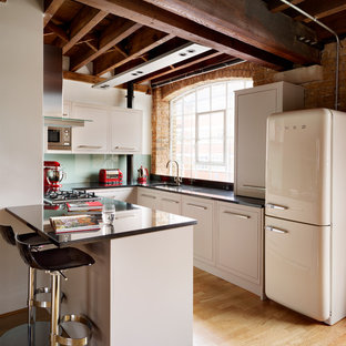 Design ideas for a small eclectic u-shaped kitchen in London with an undermount sink, flat-panel cabinets, beige cabinets, glass sheet splashback, white appliances, light hardwood floors and a peninsula.