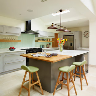 Eclectic kitchen in London with flat-panel cabinets, green splashback, subway tile splashback, stainless steel appliances and with island.
