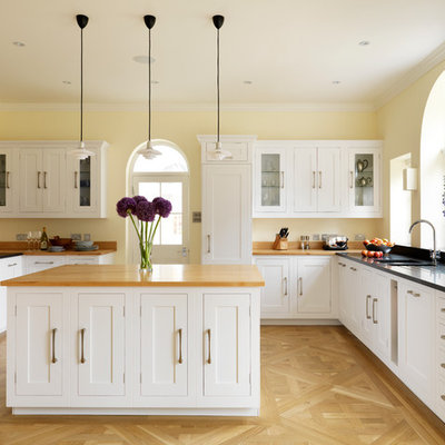 Example of a large classic u-shaped light wood floor kitchen design in London with an undermount sink, shaker cabinets, white cabinets, concrete countertops and an island