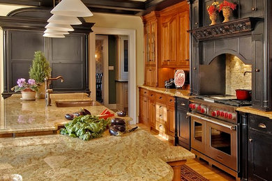 Example of a large classic l-shaped light wood floor enclosed kitchen design in Philadelphia with a farmhouse sink, shaker cabinets, black cabinets, granite countertops, beige backsplash, stone tile backsplash, paneled appliances and an island