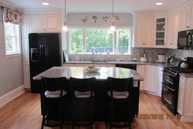 Eat-in kitchen - mid-sized traditional l-shaped medium tone wood floor eat-in kitchen idea in Philadelphia with an undermount sink, raised-panel cabinets, white cabinets, granite countertops, gray backsplash, mosaic tile backsplash, black appliances and an island