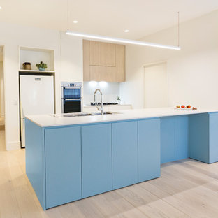 Contemporary galley open plan kitchen in Melbourne with a double-bowl sink, flat-panel cabinets, blue cabinets, wood benchtops, white splashback, white appliances, light hardwood floors, a peninsula and beige floor.