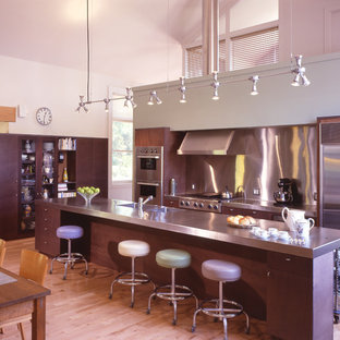 Mid-sized contemporary l-shaped eat-in kitchen in New York with an integrated sink, flat-panel cabinets, dark wood cabinets, stainless steel benchtops, metallic splashback, metal splashback, stainless steel appliances, light hardwood floors and with island.