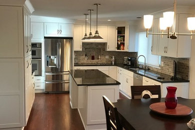 Mid-sized transitional u-shaped medium tone wood floor eat-in kitchen photo in Detroit with an undermount sink, shaker cabinets, white cabinets, granite countertops, gray backsplash, stone tile backsplash, stainless steel appliances and an island