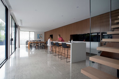 Свежая идея для дизайна: кухня-гостиная среднего размера в стиле ретро с двойной мойкой, столешницей из акрилового камня, черным фартуком, фартуком из стеклянной плитки, черной техникой, бетонным полом и островом - отличное фото интерьера