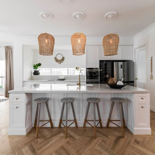 Inspiration for a large beach style galley eat-in kitchen in Brisbane with an undermount sink, marble benchtops, white splashback, marble splashback, with island, white benchtop, recessed-panel cabinets, white cabinets, black appliances, medium hardwood floors and beige floor.