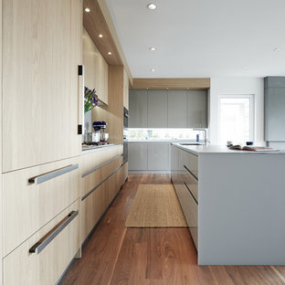 Réalisation d'une cuisine ouverte design en L de taille moyenne avec un évier encastré, un placard à porte plane, des portes de placard en bois clair, un sol en bois foncé, un îlot central, un plan de travail en verre, une crédence grise et un électroménager en acier inoxydable.
