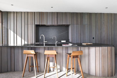 Photo of a contemporary kitchen with medium wood cabinets, granite worktops, black splashback, stainless steel appliances, a submerged sink, beaded cabinets, terrazzo flooring, an island and grey floors.