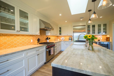 Large trendy l-shaped light wood floor enclosed kitchen photo in Orange County with an undermount sink, shaker cabinets, white cabinets, granite countertops, yellow backsplash, mosaic tile backsplash, stainless steel appliances and an island