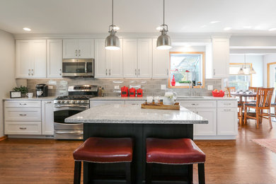Open concept kitchen - large transitional galley medium tone wood floor and brown floor open concept kitchen idea in Chicago with a double-bowl sink, shaker cabinets, white cabinets, quartz countertops, gray backsplash, ceramic backsplash, stainless steel appliances and an island