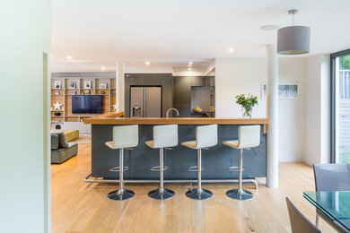 Contemporary kitchen in London with a built-in sink, flat-panel cabinets, grey cabinets, engineered stone countertops, grey splashback, ceramic splashback, stainless steel appliances, light hardwood flooring and an island.
