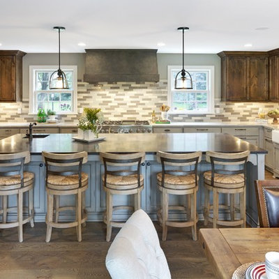 Example of a large country u-shaped brown floor and medium tone wood floor eat-in kitchen design in Minneapolis with a farmhouse sink, recessed-panel cabinets, gray cabinets, multicolored backsplash, paneled appliances, an island, solid surface countertops and porcelain backsplash