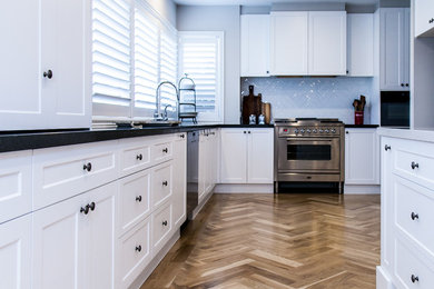 メルボルンにある高級な広いトラディショナルスタイルのおしゃれなキッチン (ドロップインシンク、シェーカースタイル扉のキャビネット、白いキャビネット、クオーツストーンカウンター、白いキッチンパネル、サブウェイタイルのキッチンパネル、シルバーの調理設備、淡色無垢フローリング、ベージュの床) の写真