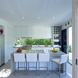 Imagen de cocina en L, contemporánea, de tamaño medio, abierta, con armarios con paneles lisos, puertas de armario blancas, electrodomésticos de acero inoxidable, una isla y suelo de terrazo