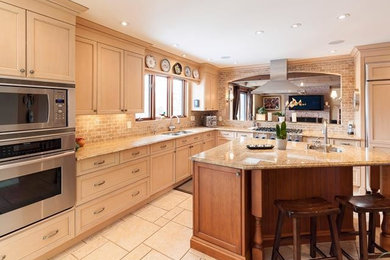 Example of a large classic l-shaped ceramic tile and beige floor kitchen design in Montreal with an undermount sink, shaker cabinets, beige cabinets, granite countertops, beige backsplash, stone tile backsplash, stainless steel appliances and an island