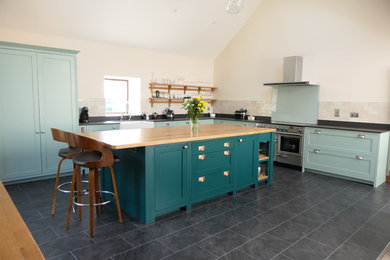 Design ideas for a large classic l-shaped open plan kitchen in West Midlands with a belfast sink, shaker cabinets, green cabinets, engineered stone countertops, grey splashback, glass sheet splashback, stainless steel appliances, ceramic flooring, an island, black floors and black worktops.