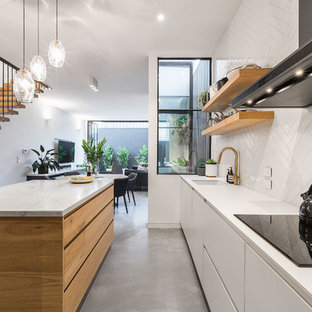 Design ideas for a mid-sized contemporary l-shaped eat-in kitchen in Melbourne with an undermount sink, flat-panel cabinets, medium wood cabinets, marble benchtops, white splashback, concrete floors, with island, grey floor, mosaic tile splashback and black appliances.
