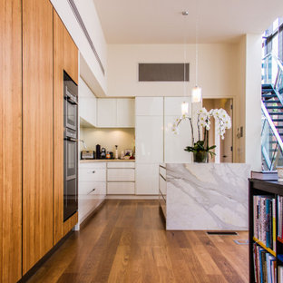 This is an example of a contemporary l-shaped kitchen in Melbourne with flat-panel cabinets, white cabinets, stainless steel appliances, medium hardwood floors, with island, brown floor and grey benchtop.