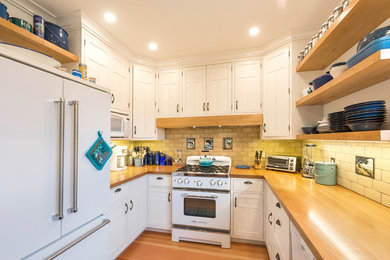 Cottage u-shaped kitchen photo in Vancouver with a farmhouse sink, recessed-panel cabinets, white cabinets, wood countertops and beige backsplash