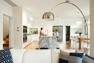Einzeilige, Große Moderne Wohnküche mit weißen Schränken, Küchenrückwand in Weiß, Glasrückwand, Küchengeräten aus Edelstahl, hellem Holzboden, Kücheninsel, flächenbündigen Schrankfronten und Granit-Arbeitsplatte in Melbourne