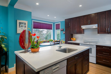 Example of a large classic l-shaped light wood floor eat-in kitchen design in Vancouver with an undermount sink, recessed-panel cabinets, dark wood cabinets, white backsplash and white appliances