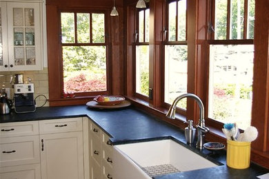 Example of a large cottage l-shaped medium tone wood floor enclosed kitchen design in Vancouver with a farmhouse sink, shaker cabinets, white cabinets, soapstone countertops, ceramic backsplash, stainless steel appliances and an island