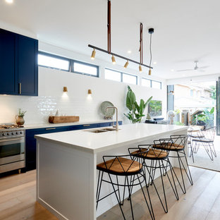 Photo of a contemporary galley eat-in kitchen in Sydney with an undermount sink, shaker cabinets, black cabinets, white splashback, stainless steel appliances, medium hardwood floors, with island, brown floor and white benchtop.