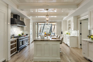This is an example of a large traditional u-shaped enclosed kitchen in New York with a submerged sink, recessed-panel cabinets, white cabinets, stainless steel appliances, light hardwood flooring, an island, white splashback, marble splashback and beige floors.