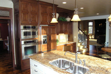 Example of a mid-sized classic l-shaped medium tone wood floor and brown floor eat-in kitchen design in Other with a double-bowl sink, raised-panel cabinets, medium tone wood cabinets, granite countertops, stainless steel appliances and an island