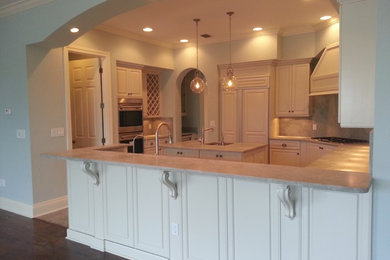 Inspiration for a transitional u-shaped ceramic tile and beige floor enclosed kitchen remodel in Tampa with an undermount sink, raised-panel cabinets, white cabinets, granite countertops, beige backsplash, stone slab backsplash, stainless steel appliances and an island