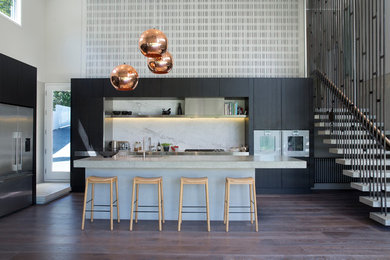 Trendy l-shaped medium tone wood floor kitchen photo in Auckland with flat-panel cabinets, black cabinets, white backsplash, stone slab backsplash, an island and stainless steel appliances