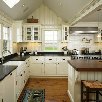Example of a large cottage l-shaped medium tone wood floor open concept kitchen design in Boston with a farmhouse sink, glass-front cabinets, white cabinets, white backsplash, subway tile backsplash, stainless steel appliances, an island and black countertops