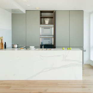 Diseño de cocina en U, contemporánea, pequeña, con armarios con paneles lisos, salpicadero de vidrio templado, suelo de madera clara, fregadero bajoencimera, puertas de armario verdes y península