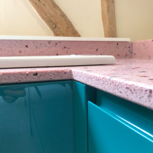 Bild på ett litet funkis rosa rosa kök, med släta luckor, blå skåp, bänkskiva i återvunnet glas och rostfria vitvaror