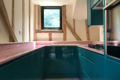 Modelo de cocina moderna pequeña con armarios con paneles lisos, puertas de armario azules, encimera de vidrio reciclado, electrodomésticos de acero inoxidable y encimeras rosas