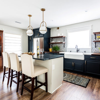 Example of a mid-sized country l-shaped laminate floor and brown floor open concept kitchen design in Los Angeles with a farmhouse sink, raised-panel cabinets, blue cabinets, wood countertops, blue backsplash, cement tile backsplash, stainless steel appliances, an island and brown countertops