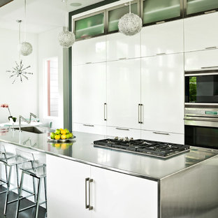 Modelo de cocina comedor de galera, actual, con fregadero integrado, armarios con paneles lisos, puertas de armario blancas, encimera de acero inoxidable y electrodomésticos de acero inoxidable
