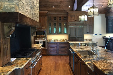 Example of a large tuscan u-shaped medium tone wood floor and brown floor open concept kitchen design in Other with a single-bowl sink, beaded inset cabinets, dark wood cabinets, granite countertops, black backsplash, stainless steel appliances, an island and brown countertops